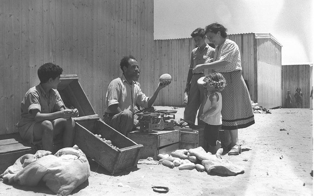 Eine Immigrantin aus Bessarabien (heute Moldau, Ukraine) kauf Lebensmittel bei Eliahu Abraham, ehemals ein Schauspieler aus Baghdad. Ma'abara (Flüchtlingslager) in Kiryat Ono, Israel 1951. Foto:GPO