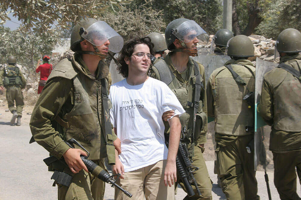 Yossis Festnahme während einer Demonstration gegen den Bau der Sperranlage im Dorf Bil'in in der Westbank, 2005. Auf seinem T-Shirt steht auf Hebräisch: „So sieht eine Feministin aus.“